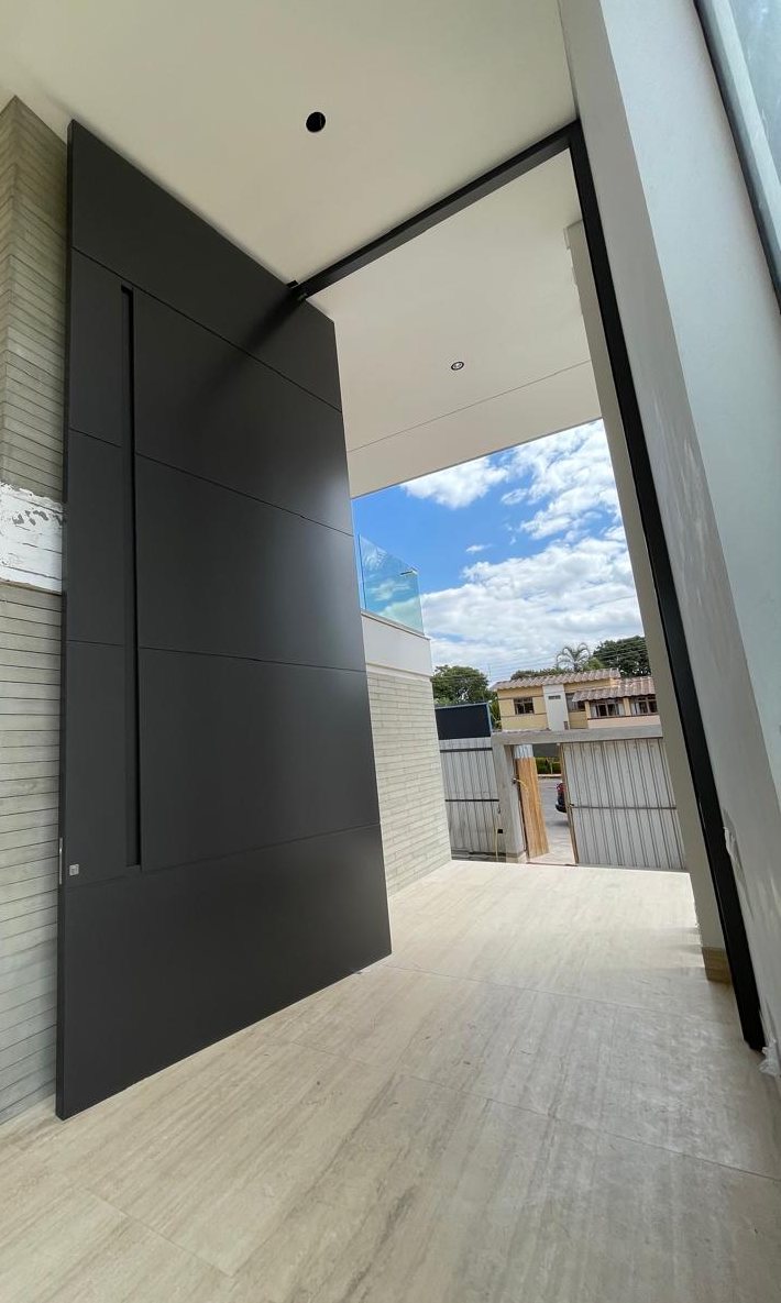Porta pivotante em ACM na entrada de uma residência, com folha escura de piso a teto